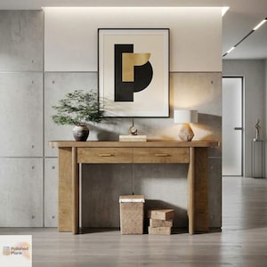 May include: A light brown wooden console table with two drawers and brass handles. A framed abstract art piece hangs above the table, along with a small lamp, a potted plant, and decorative items. A woven basket and two small wooden blocks sit below the table.