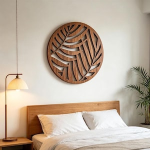 Puede incluir: Una pieza de arte mural circular de madera con un diseño cortado con láser de hojas de palma superpuestas. La veta de madera marrón natural es visible en todo el intrincado patrón calado, montado centralmente en una pared blanca lisa.