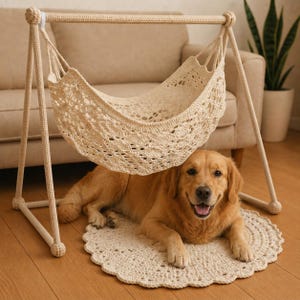May include: A cream-colored crocheted pet hammock suspended from a matching A-frame stand, featuring an intricate openwork pattern. A golden retriever dog lies on a circular, matching crocheted mat directly underneath the hanging hammock structure.