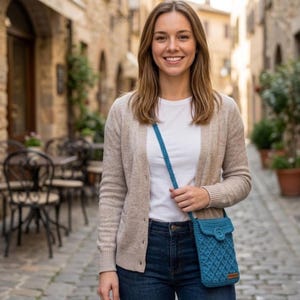 "Smiling woman standing on a cobblestone street wearing a teal crochet crossbody phone bag with button closure"