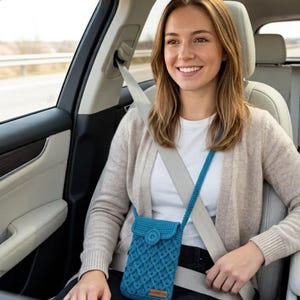 "Smiling woman sitting in a car wearing a teal crochet crossbody phone pouch with button closure"
