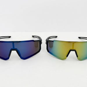 May include: Two pairs of sport sunglasses with a sleek, modern design. One pair features blue lenses, the other has yellow-green lenses. Both have black frames and a wraparound style, suitable for outdoor activities.