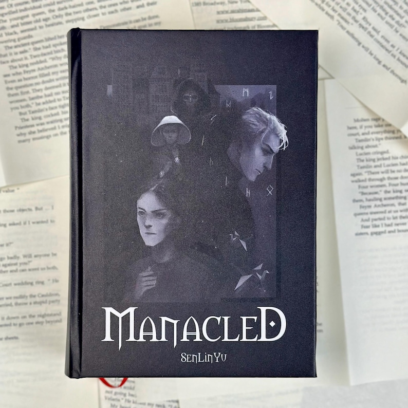 May include: A hardcover book titled "Manacled" by SenLinYu. The cover features a grayscale illustration of several figures with a gothic aesthetic. The book is black with white lettering.