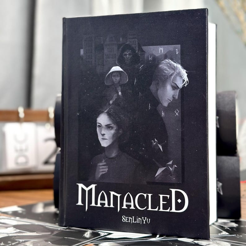 May include: A hardcover book with a black cover featuring illustrations of several people. The title "Manacled" is in white gothic lettering, with the author's name, SenLinYu, below. The book's spine is white.