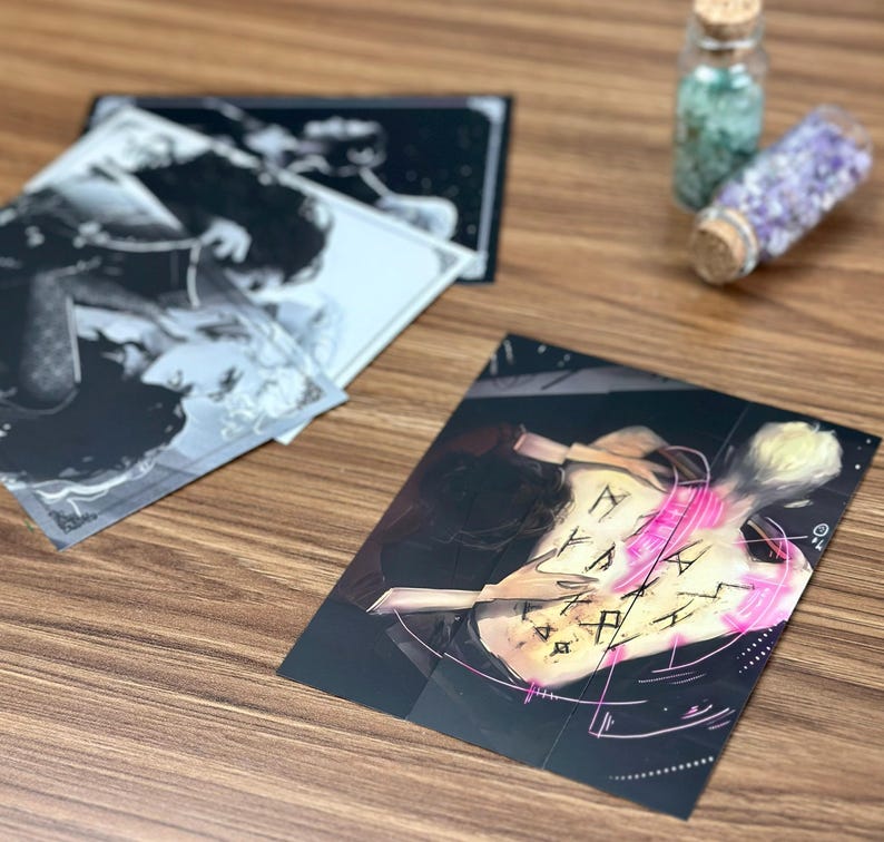 May include: A collection of art prints featuring black and white illustrations and a color print with a figure and symbols. Two small glass bottles with cork stoppers are also visible.