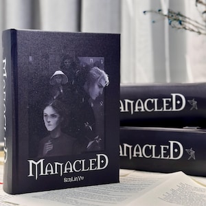 May include: A black book titled "Manacled" with a dark illustration of three people. The book's cover features the author's name, SenLinYu, in white text. Additional books with the same title are stacked in the background.