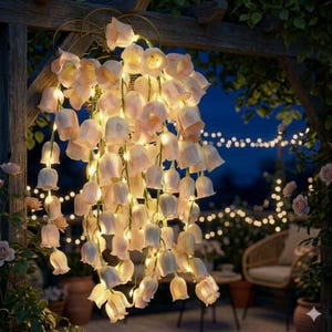 以下が含まれることがあります： 木製のパーゴラから吊り下げられた、淡いピンクと白の花の形をした装飾的なストリングライト。 ライトは点灯し、暖かく魅力的な輝きを生み出しています。 屋外のシーンにはバラの茂みと籐の椅子があり、夕暮れ時の庭を連想させます。