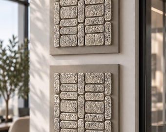 May include: Two square wall art pieces featuring a grid of raised, rectangular blocks with a rough, stone-like texture. The blocks are arranged in a repeating pattern on a smooth, light beige base, creating a three-dimensional geometric design.