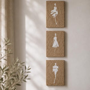 Peut inclure: Trois œuvres d'art murales rectangulaires avec une surface texturée et brune. Chacune présente une illustration blanche et minimaliste d'une robe. L'art est exposé sur un mur de couleur neutre, créant une esthétique moderne et artistique.