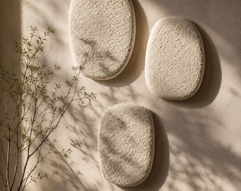 May include: Three oval-shaped wall art pieces with a textured, off-white surface. The pieces are arranged in a cluster on a neutral-toned wall. Each piece features a rough, organic finish that creates subtle shadows and depth across the surface.
