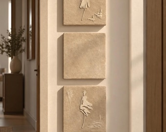May include: Three square, beige, textured wall art panels arranged vertically. The top and bottom panels feature a raised, white, abstract silhouette of a figure in a dress, while the middle panel is a plain, solid, textured beige square.