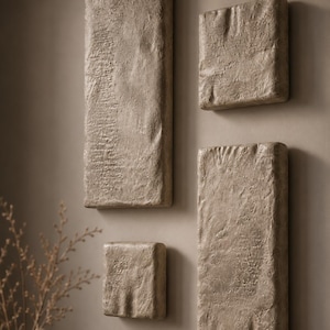 Può includere: Quattro pezzi di arte murale rettangolari e strutturati di varie dimensioni. L'arte ha un colore beige neutro e una superficie ruvida e irregolare, creando un'estetica naturale e terrosa. I pezzi sono montati su una parete dai toni neutri, aggiungendo un tocco di arredamento minimalista.