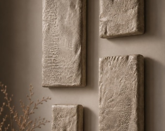 May include: Four textured, rectangular wall art pieces in varying sizes. The art has a neutral, beige color and a rough, uneven surface, creating a natural, earthy aesthetic. The pieces are mounted on a neutral-toned wall, adding a touch of minimalist decor.