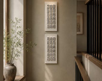 May include: Two vertical rectangular wall art pieces featuring a grid of small, textured, off-white square tiles. Each piece contains four rows of four raised, weathered-looking squares mounted on a smooth, flat, rectangular off-white panel.