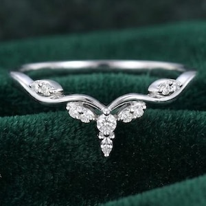 Op de afbeelding: Een zilverkleurige ring met een gebogen ontwerp, versierd met meerdere kleine, sprankelende diamanten. De ring heeft een centrale cluster van diamanten en extra stenen langs de gebogen band, tegen een donkergroene achtergrond.