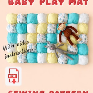 May include: A rectangular baby play mat sewing pattern featuring a grid of stuffed fabric squares in yellow, turquoise, and a white print with small blue illustrations. A brown plush monkey and a gray crocheted rabbit rest on the mat. Text reads BABY PLAY MAT, With video instructions, and SEWING PATTERN, with a PDF icon.