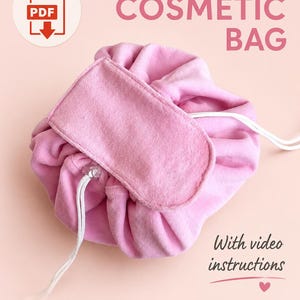 Puede incluir: Un neceser cosmético rosa con cordón, solapa rectangular y cierre de cordón blanco. El texto dice DRAWSTRING COSMETIC BAG, With video instructions y SEWING PATTERN. Un icono de PDF es visible en la esquina superior izquierda de la imagen.