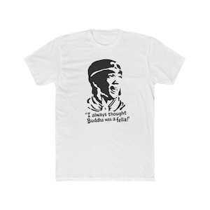 May include: White t-shirt with a black graphic of a man's face and the quote, "I always thought Buddha was a fella!" The graphic is a stylized illustration. The shirt is a crew neck style.