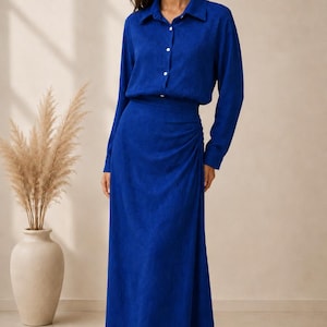 May include: A vibrant cobalt blue two-piece ensemble, comprising a long-sleeved shirt with buttons and a coordinating wrap skirt. The outfit is crafted from a textured material. The skirt reaches the ankles.
