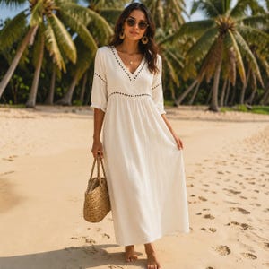 Peut inclure: Une robe longue maxi blanc cassé avec un décolleté en V, des manches trois-quarts et une taille froncée. La robe est ornée de bordures brodées noires le long de l'encolure, des manches et de la taille, accompagnée d'un sac cabas en paille tressée.