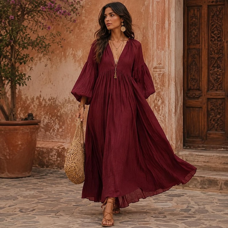 K&ouml;nnte beinhalten: Ein tiefburgunderrotes Maxikleid mit tiefem V-Ausschnitt, langen, volumin&ouml;sen Bischofs&auml;rmeln mit gerafften B&uuml;ndchen und einem flie&szlig;enden, bodenlangen Rock. Das Kleid wird mit einer gewebten beigen Tragetasche und braunen Riemchensandalen kombiniert.