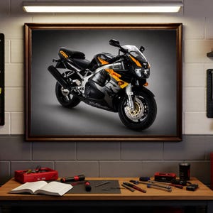 May include: Framed image of a black and yellow sport motorcycle. The motorcycle is displayed in a workshop setting, with tools and equipment visible in the background. The motorcycle has a sleek design with a black frame and yellow accents.