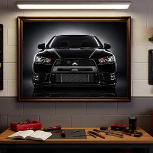 May include: A framed wall art print featuring the front view of a black Mitsubishi Lancer Evolution saloon. The car is centred with its headlights and grille clearly visible against a dark background, displayed in a workshop setting.