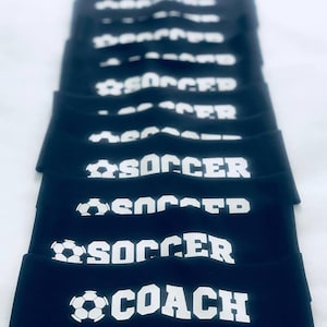 以下が含まれることがあります： 白いサッカーボールと「SOCCER」または「SOCCER COACH」の文字が書かれた黒いヘッドバンドのスタックです。