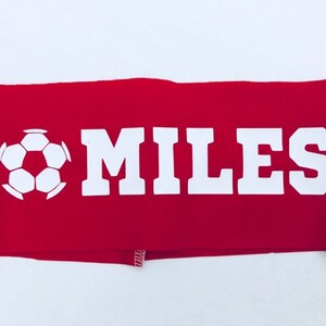 以下が含まれることがあります： 白いサッカーボールと白い文字で「MILES」と書かれた赤い布製のヘッドバンド