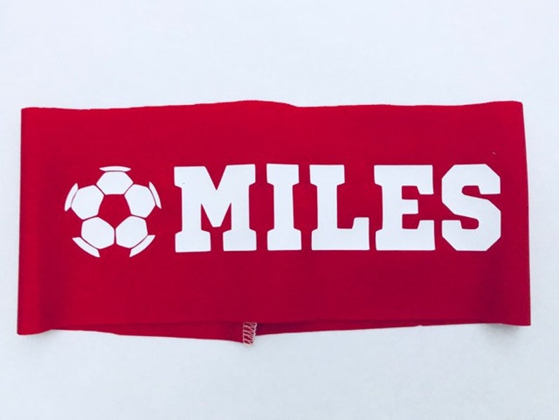 以下が含まれることがあります： 白いサッカーボールと白い文字で「MILES」と書かれた赤い布製のヘッドバンド