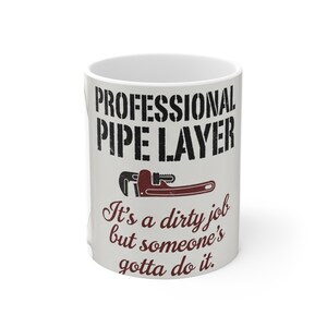 May include: White ceramic mug with the text "PROFESSIONAL PIPE LAYER" in black, along with a graphic of a wrench. Below the graphic is the phrase "It's a dirty job but someone's gotta do it."