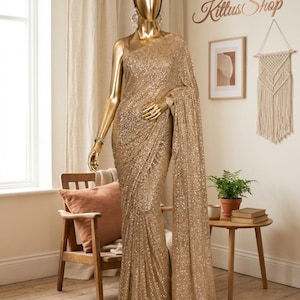 May include: A gold sequin saree draped on a gold mannequin. The saree features dense, shimmering gold sequins covering the entire fabric, including the pallu which hangs down from the shoulder. The mannequin has a smooth, metallic gold finish.