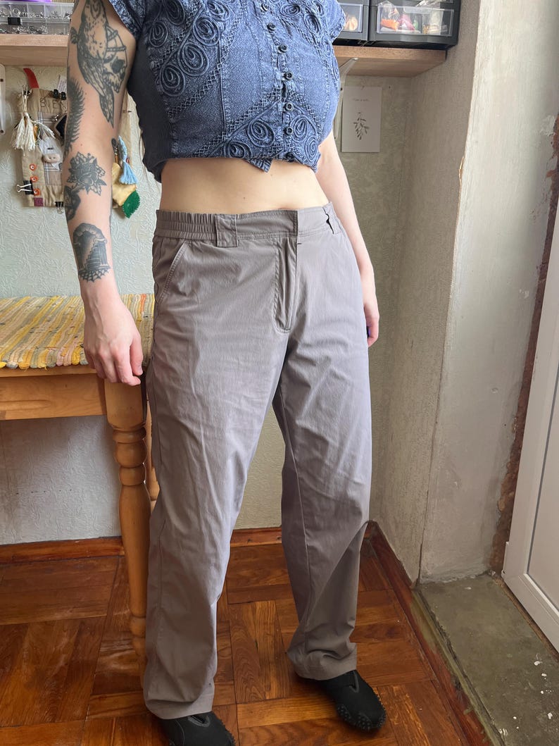 Op de afbeelding: Een effen taupekleurige broek met een platte voorkant, een knoop- en ritssluiting en een elastische tailleband. De broek heeft een recht model met zijzakken en is gemaakt van een glad, lichtgewicht materiaal.