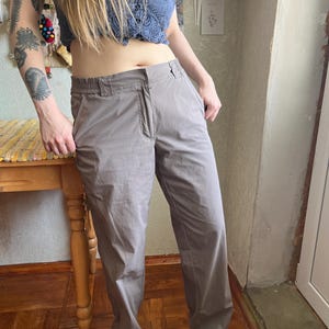 Op de afbeelding: Een effen taupekleurige broek met een rechte snit, een standaard tailleband met riemlussen, een ritssluiting aan de voorzijde en zijzakken. De broek is gemaakt van een gladde, lichtgewicht stof met een subtiele glans.