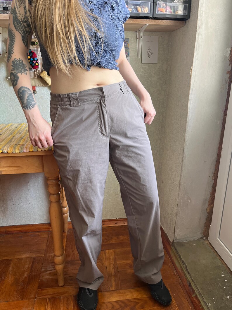 Op de afbeelding: Een effen taupekleurige broek met een rechte snit, een standaard tailleband met riemlussen, een ritssluiting aan de voorzijde en zijzakken. De broek is gemaakt van een gladde, lichtgewicht stof met een subtiele glans.