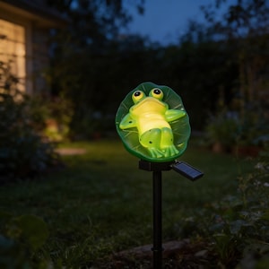 May include: A solar-powered garden stake featuring a frog resting on a lily pad. The frog is yellow and green, with black eyes, and the lily pad is green. The stake is black, and the solar panel is attached below the lily pad.