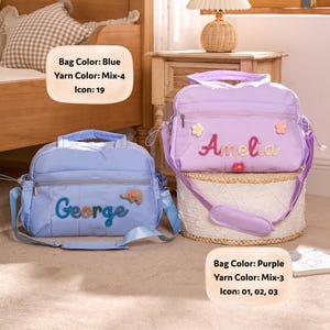 K&ouml;nnte beinhalten: Zwei personalisierte Baby-Taschen. Eine ist hellblau mit "George" in blauer Wolle gestickt und einem Elefanten-Symbol. Die andere ist lila mit "Amelia" in rosa Wolle gestickt und Blumen-Symbolen. Beide haben Schultergurte.