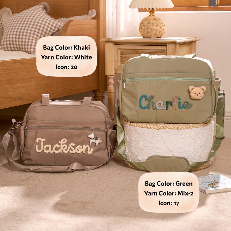 K&ouml;nnte beinhalten: Zwei Wickeltaschen. Eine ist khaki mit dem Namen "Jackson" in wei&szlig;em Garn gestickt und einem Pferde-Symbol. Die andere ist gr&uuml;n mit "Charlie" in Blau gestickt und einem Teddyb&auml;r-Symbol. Beide haben Schultergurte.