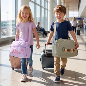 May include: A light purple shoulder bag with the name Alice and a small flower patch, and a sage green shoulder bag with the name George and a small red car patch. Both bags feature a rectangular shape, zippered front pockets, and adjustable straps.
