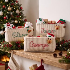 Könnte beinhalten: Drei cremefarbene Aufbewahrungskörbe aus Kord mit braunen Seitengriffen. Jeder Korb ist mit einem personalisierten Namen in rot-weiß gestreiften Buchstaben im Zuckerstangen-Design und einer kleinen Filzapplikation versehen.