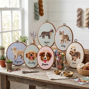 May include: Embroidered pet portraits in oval hoops, featuring dogs and a cat, each with a name beneath. The hoops are displayed on a wooden table, with craft supplies visible in the background.