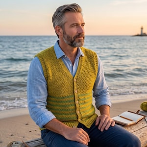 May include: A mustard yellow knit button-down vest featuring a textured stitch pattern and horizontal green stripes at the bottom, worn over a light blue long-sleeved collared shirt with dark blue trousers.