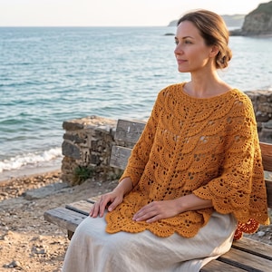 May include: A mustard yellow crochet poncho featuring an intricate leaf-like pattern with a scalloped hemline. The garment has a wide, rounded neckline and drapes over the shoulders, showcasing a detailed openwork texture throughout the fabric.