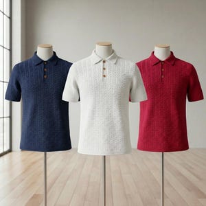 Puede incluir: Tres polos de manga corta en azul marino, blanco y rojo, expuestos en maniquíes. Cada camisa presenta un patrón de punto texturizado, un cuello y botones de madera. Las camisas se presentan sobre soportes plateados.