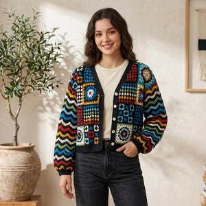 May include: A colorful, button-down cardigan with a patchwork design. The sweater features a variety of geometric patterns in shades of blue, red, yellow, and black. The sleeves have a wavy pattern. The cardigan is worn over a white shirt and black jeans.