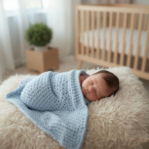 May include: A sleeping newborn wrapped in a light blue crocheted blanket. The baby rests on a fluffy, white, faux fur surface. A wooden crib is visible in the background, suggesting a nursery setting.