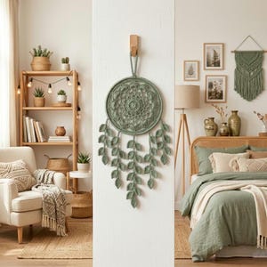 May include: A sage green, handmade dreamcatcher with a circular, lacy design and leaf-shaped pendants. The dreamcatcher hangs on a white wall, complementing the neutral tones of the room's decor, including a wooden shelf with plants and a cozy armchair.