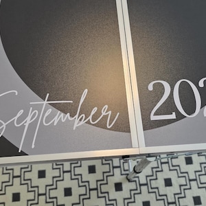 May include: A dark gray and black folding table surface featuring a circular design with the white text 5. September 2026 printed across the center. The table has a metallic silver frame and a visible seam running vertically through the middle.
