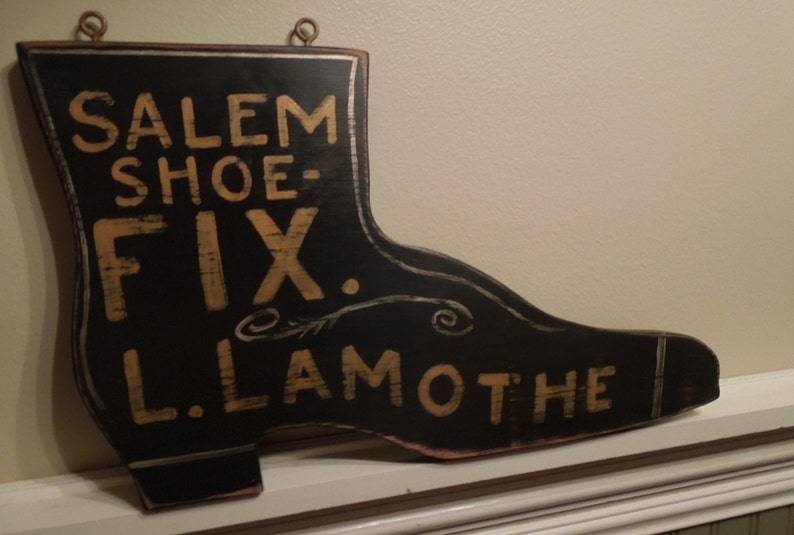 May include: A black wooden shoe-shaped sign with gold lettering that reads "Salem Shoe-Fix L. Lamothe".