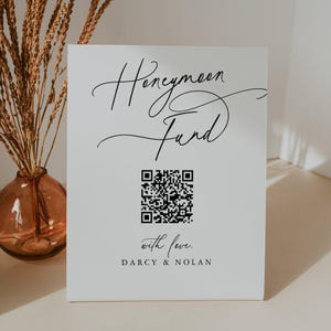 Op de afbeelding: Een wit rechthoekig bord met de zwarte tekst Honeymoon Fund in een cursief lettertype, een centrale zwart-witte QR-code, de tekst with love. in cursief, en de namen DARCY & NOLAN in een strak, schreefloos hoofdlettertype.